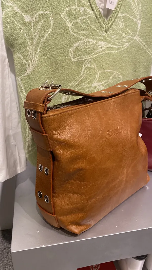 Cartera Agostina suela sobre una mesa, entre ropa